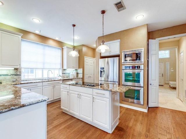 kitchen with light stone countertops, a center island, decorative light fixtures, stainless steel appliances, and white cabinetry