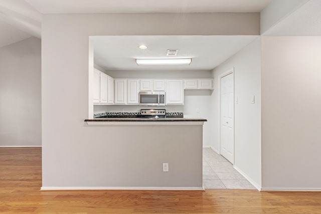 kitchen with kitchen peninsula, range, light wood-type flooring, and white cabinetry