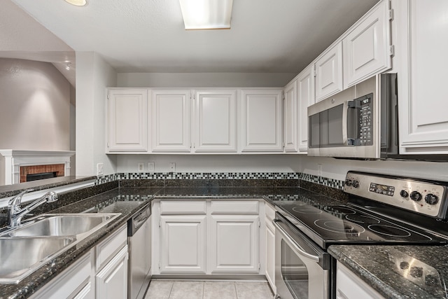 kitchen with white cabinetry, dark stone counters, a fireplace, light tile patterned floors, and appliances with stainless steel finishes