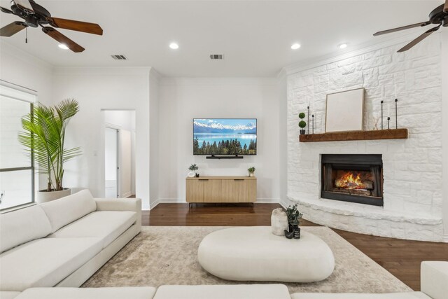 living room with hardwood / wood-style flooring, ornamental molding, a stone fireplace, and ceiling fan