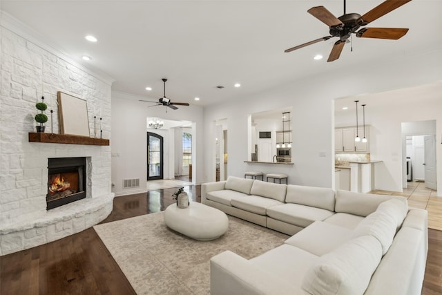 living room with a stone fireplace, ceiling fan, light wood-type flooring, ornamental molding, and washer / dryer