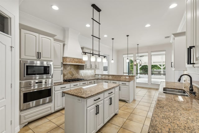 kitchen with appliances with stainless steel finishes, premium range hood, sink, decorative light fixtures, and white cabinetry