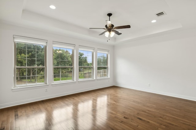 empty room with wood-type flooring, a raised ceiling, ceiling fan, and ornamental molding