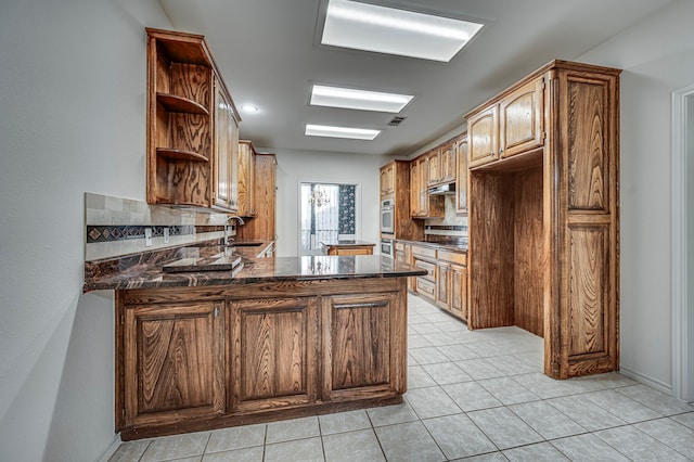 kitchen with dark stone countertops, kitchen peninsula, sink, and tasteful backsplash