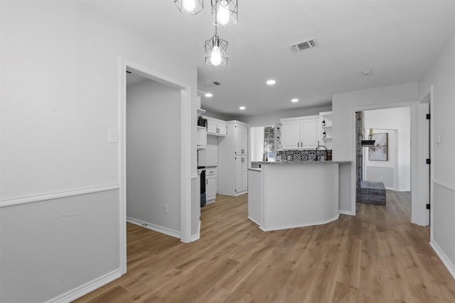 kitchen featuring kitchen peninsula, dark stone counters, pendant lighting, light hardwood / wood-style floors, and white cabinetry