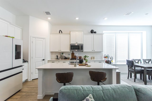 kitchen featuring white cabinetry, an island with sink, appliances with stainless steel finishes, and light hardwood / wood-style flooring