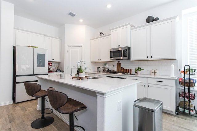 kitchen with appliances with stainless steel finishes, a kitchen island with sink, sink, white cabinets, and light hardwood / wood-style floors