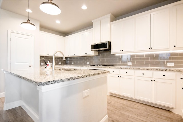 kitchen featuring an island with sink, decorative light fixtures, sink, and white cabinets