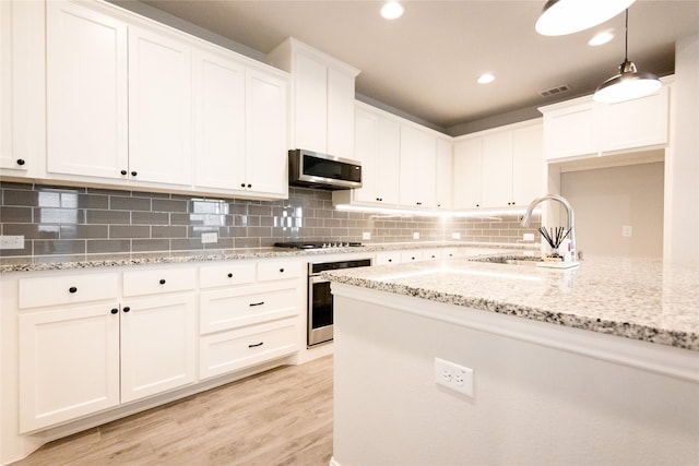 kitchen with stainless steel appliances, white cabinetry, sink, and decorative light fixtures