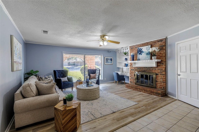 living room featuring ornamental molding, ceiling fan, light hardwood / wood-style floors, a brick fireplace, and a textured ceiling