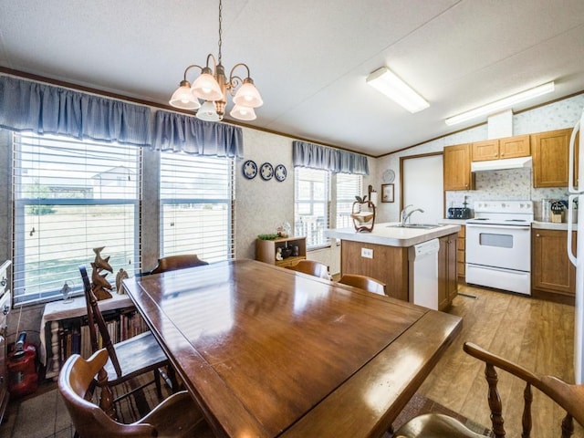 kitchen with an inviting chandelier, an island with sink, pendant lighting, white appliances, and light wood-type flooring