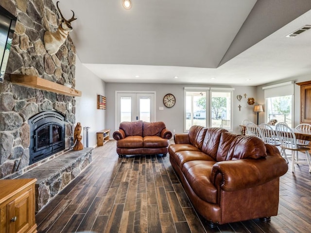 living room with a stone fireplace, dark hardwood / wood-style flooring, lofted ceiling, and french doors