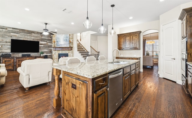 kitchen featuring ceiling fan, sink, stainless steel appliances, a stone fireplace, and an island with sink