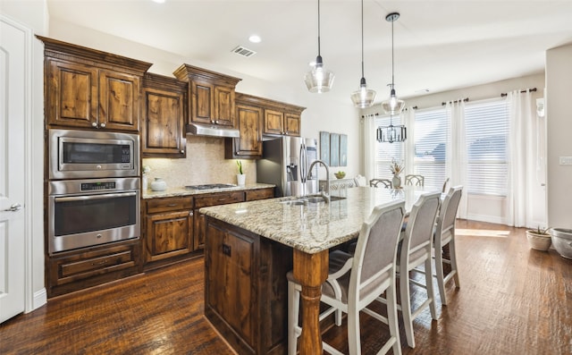 kitchen featuring pendant lighting, a kitchen island with sink, sink, tasteful backsplash, and stainless steel appliances