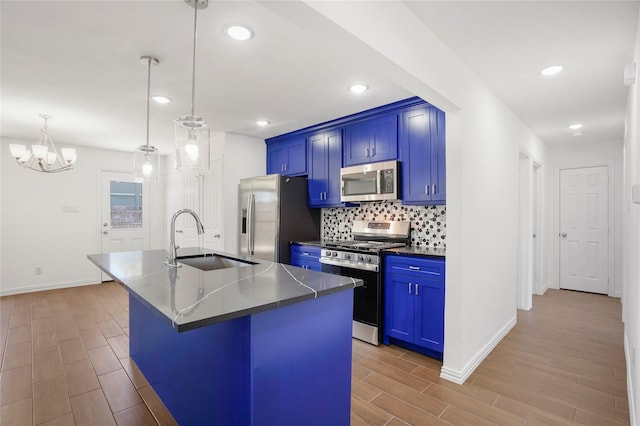 kitchen with a kitchen island with sink, appliances with stainless steel finishes, pendant lighting, sink, and blue cabinets