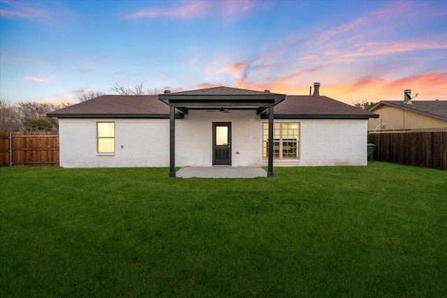 back house at dusk featuring a patio and a lawn