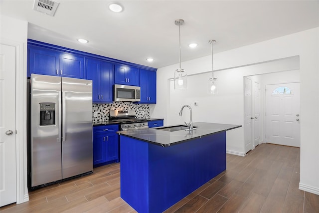 kitchen with stainless steel appliances, sink, decorative light fixtures, blue cabinetry, and a center island with sink