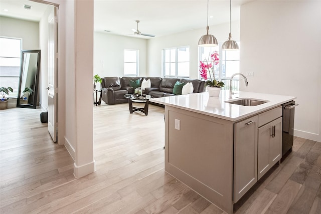 kitchen featuring pendant lighting, sink, stainless steel dishwasher, a center island with sink, and light hardwood / wood-style flooring