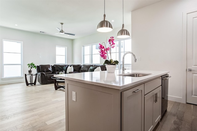 kitchen with decorative light fixtures, dishwasher, sink, a kitchen island with sink, and light hardwood / wood-style flooring