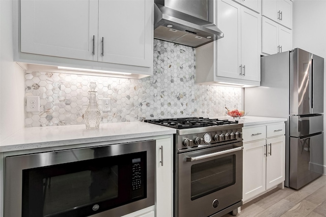 kitchen featuring white cabinetry, tasteful backsplash, light wood-type flooring, appliances with stainless steel finishes, and wall chimney range hood