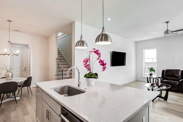 kitchen featuring sink, decorative light fixtures, light stone countertops, and a center island with sink