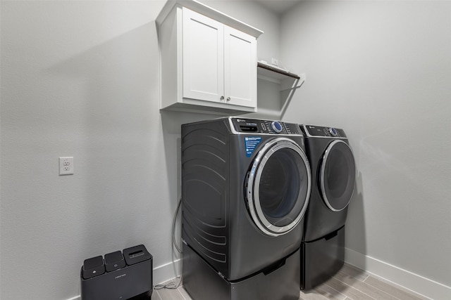 laundry room featuring cabinets, washing machine and clothes dryer, and light hardwood / wood-style floors