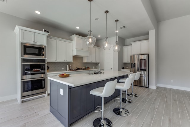 kitchen featuring appliances with stainless steel finishes, white cabinetry, sink, hanging light fixtures, and a kitchen island with sink