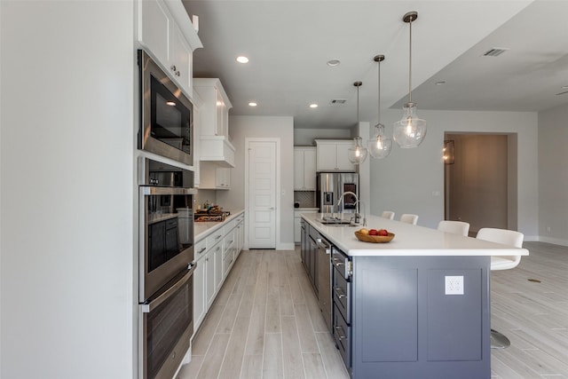 kitchen featuring decorative light fixtures, appliances with stainless steel finishes, a large island, light hardwood / wood-style floors, and white cabinets