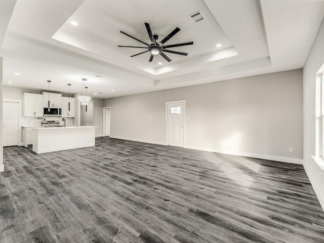 unfurnished living room featuring a raised ceiling, ceiling fan, and dark hardwood / wood-style flooring