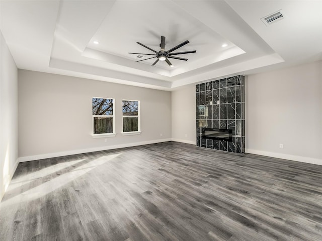 unfurnished living room featuring a tray ceiling, ceiling fan, a fireplace, and hardwood / wood-style flooring