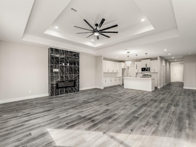 unfurnished living room featuring a raised ceiling, a premium fireplace, ceiling fan, and hardwood / wood-style flooring