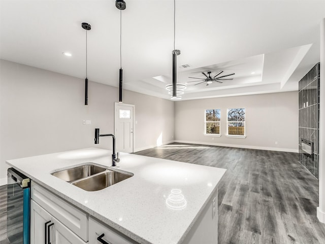 kitchen featuring a tray ceiling, a kitchen island with sink, sink, white cabinets, and hanging light fixtures