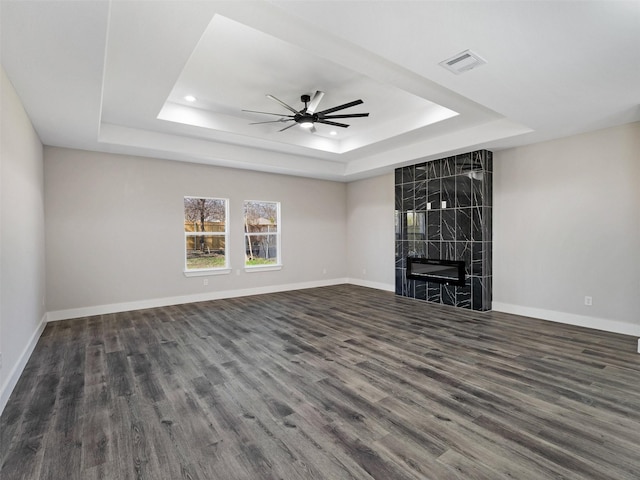 unfurnished living room featuring dark hardwood / wood-style flooring, a tray ceiling, ceiling fan, and a premium fireplace