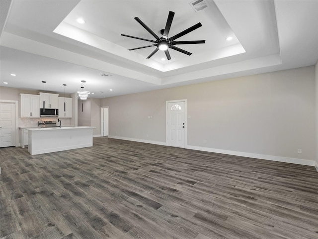 unfurnished living room with ceiling fan, dark wood-type flooring, and a tray ceiling