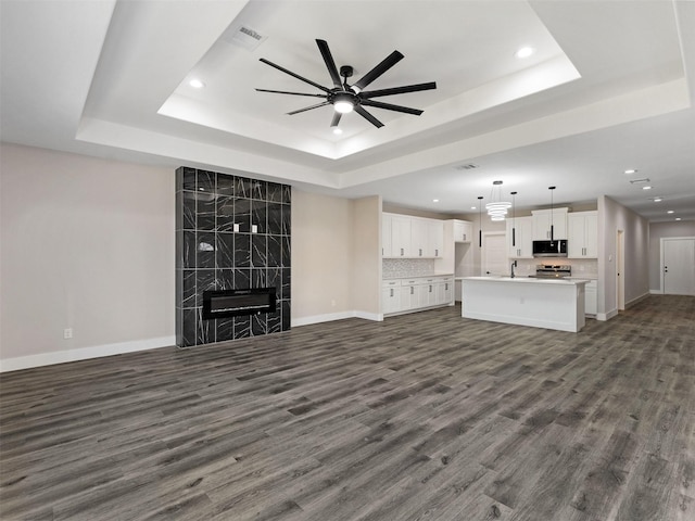 unfurnished living room with a fireplace, a tray ceiling, dark hardwood / wood-style floors, and ceiling fan