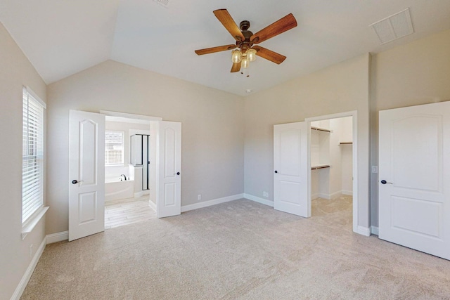 unfurnished bedroom featuring lofted ceiling, ensuite bath, ceiling fan, a spacious closet, and light colored carpet