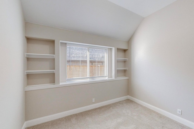 carpeted spare room featuring built in shelves and vaulted ceiling