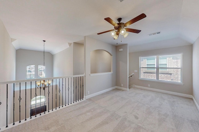 empty room featuring light carpet, ceiling fan with notable chandelier, a healthy amount of sunlight, and vaulted ceiling