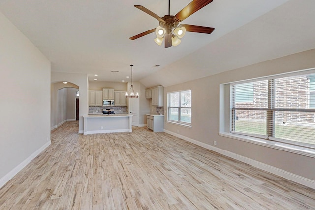 unfurnished living room featuring lofted ceiling, ceiling fan with notable chandelier, and light wood-type flooring