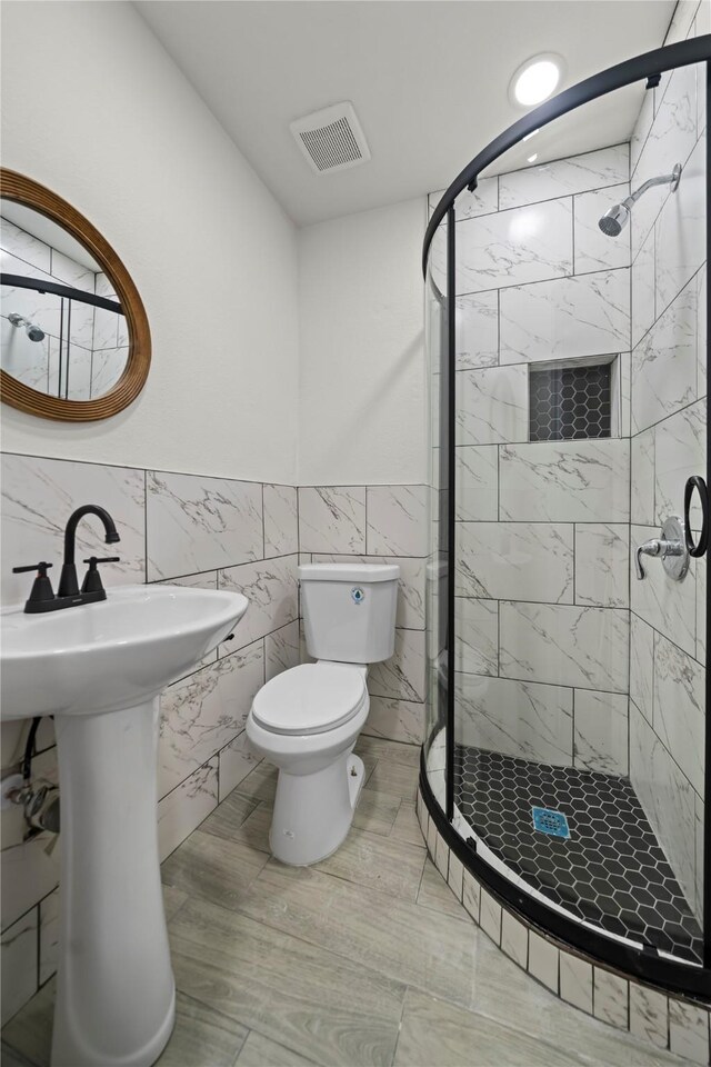 bathroom with a tile shower, tile walls, and toilet