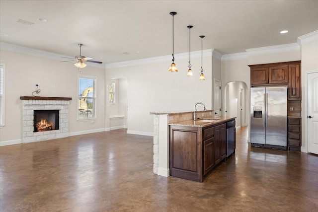 kitchen with a kitchen island with sink, ornamental molding, a fireplace, appliances with stainless steel finishes, and decorative light fixtures