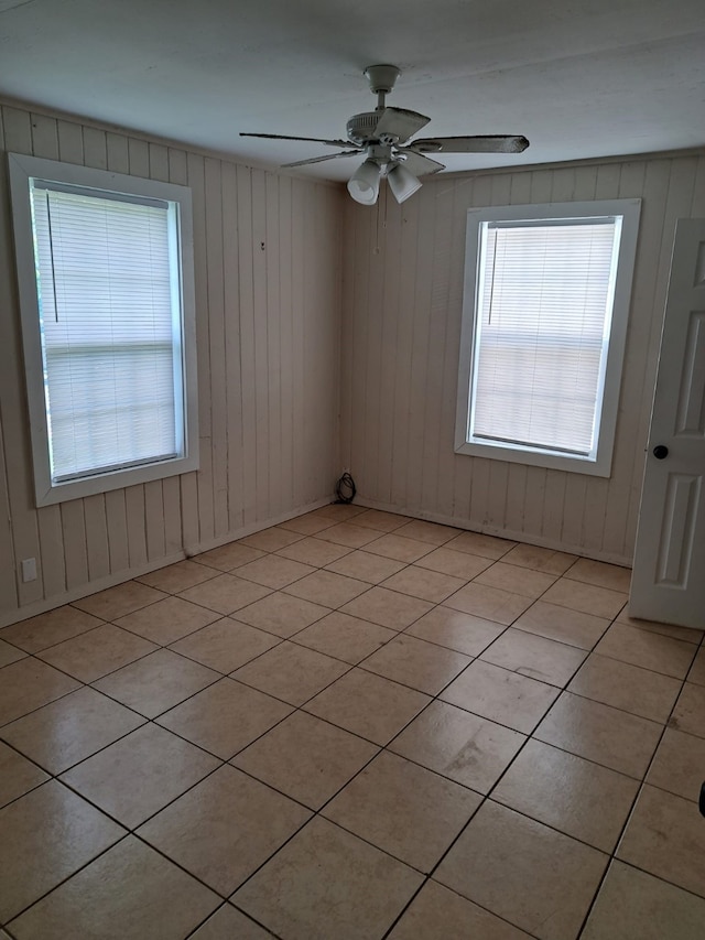 empty room with ceiling fan, wooden walls, and light tile patterned flooring