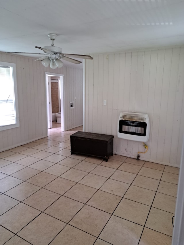 unfurnished living room with heating unit, ceiling fan, wooden walls, and light tile patterned flooring