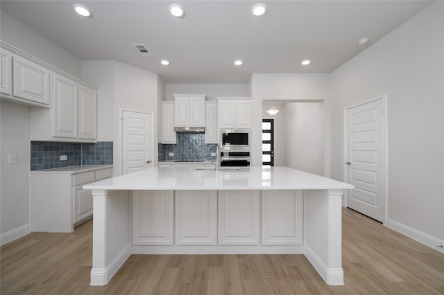 kitchen featuring white cabinets, a kitchen island with sink, appliances with stainless steel finishes, and tasteful backsplash