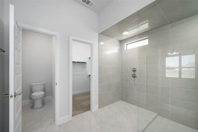 bathroom with a tile shower, toilet, and tile patterned floors