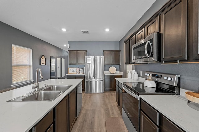 kitchen with sink, light stone countertops, light wood-type flooring, appliances with stainless steel finishes, and dark brown cabinetry