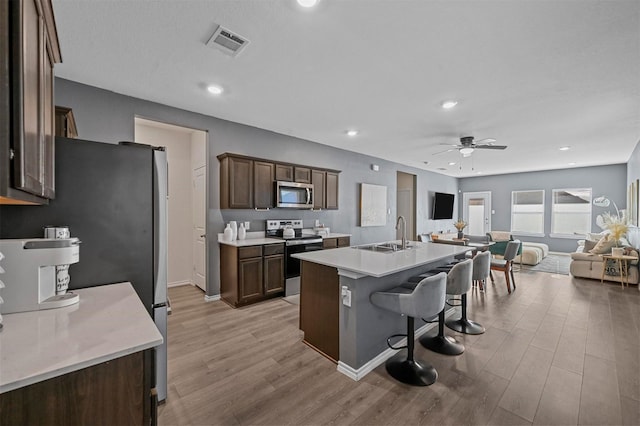 kitchen featuring a center island with sink, sink, ceiling fan, light wood-type flooring, and stainless steel appliances