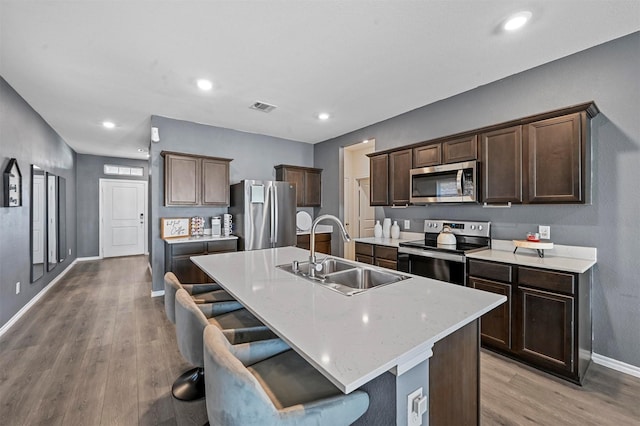 kitchen featuring a kitchen island with sink, a kitchen bar, sink, and appliances with stainless steel finishes