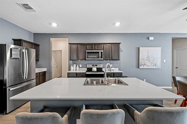 kitchen featuring a kitchen island with sink, sink, light hardwood / wood-style flooring, and appliances with stainless steel finishes