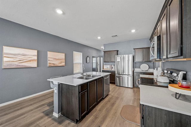 kitchen featuring dark brown cabinetry, sink, a center island with sink, stainless steel appliances, and light hardwood / wood-style floors